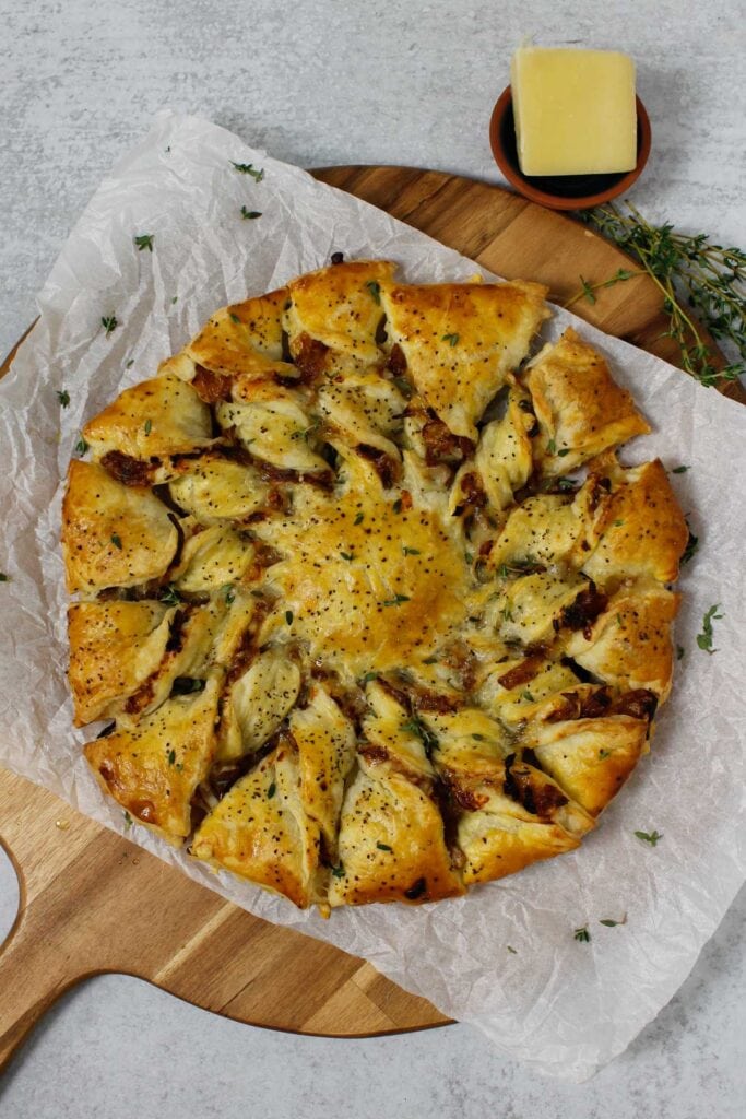 Caramelized French Onion Puff Pastry Twist on parchment paper surrounded by thyme and gruyere cheese.