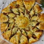 Caramelized French Onion Puff Pastry Twist on parchment paper surrounded by thyme and gruyere cheese.