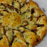 Caramelized French Onion Puff Pastry Twist on parchment paper surrounded by thyme and gruyere cheese.