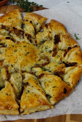 Caramelized French Onion Puff Pastry Twist on parchment paper surrounded by thyme and gruyere cheese.