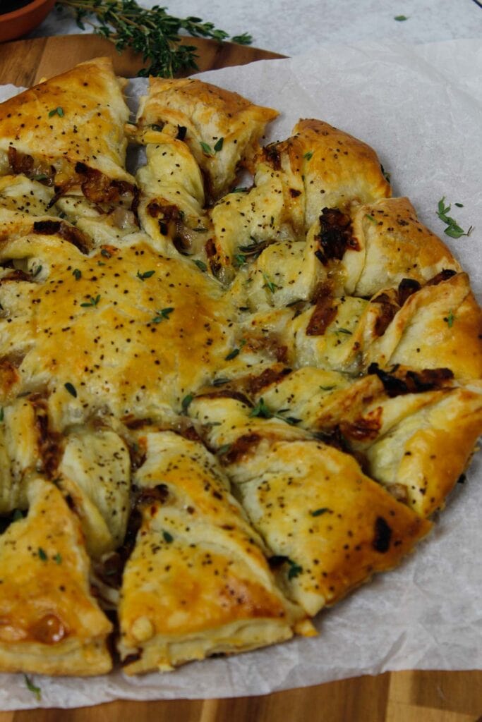 Caramelized French Onion Puff Pastry Twist on parchment paper surrounded by thyme and gruyere cheese.