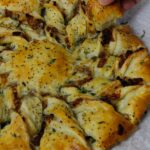 Caramelized French Onion Puff Pastry Twist on parchment paper surrounded by thyme and gruyere cheese.