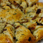 Caramelized French Onion Puff Pastry Twist on parchment paper surrounded by thyme and gruyere cheese.