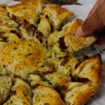 Caramelized French Onion Puff Pastry Twist on parchment paper surrounded by thyme and gruyere cheese.