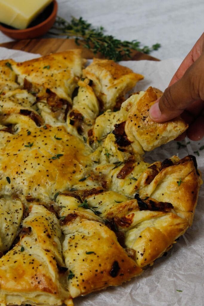 Caramelized French Onion Puff Pastry Twist on parchment paper surrounded by thyme and gruyere cheese.