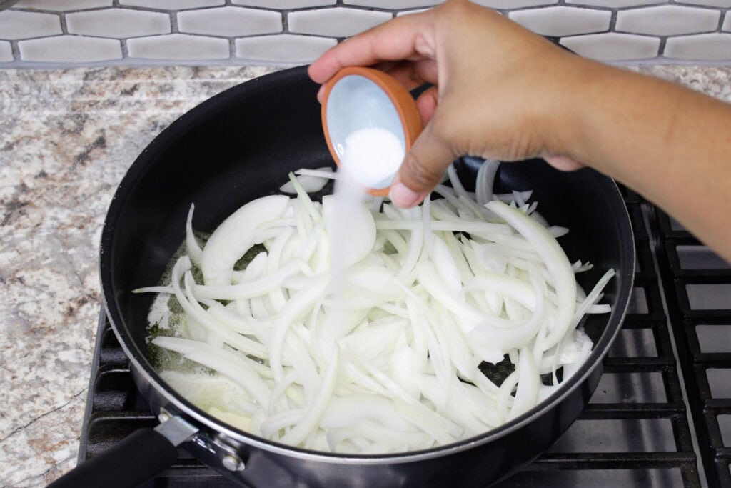 Pouring sugar over slicied onions in a nonstick skillet.