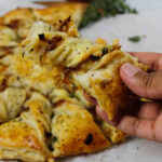 Caramelized French Onion Puff Pastry Twist on parchment paper surrounded by thyme and gruyere cheese.