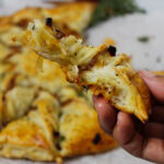 Caramelized French Onion Puff Pastry Twist on parchment paper surrounded by thyme and gruyere cheese.