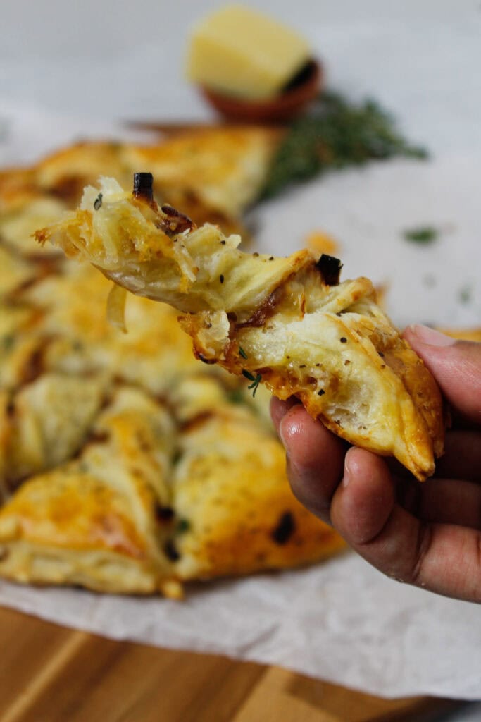 Caramelized French Onion Puff Pastry Twist on parchment paper surrounded by thyme and gruyere cheese.