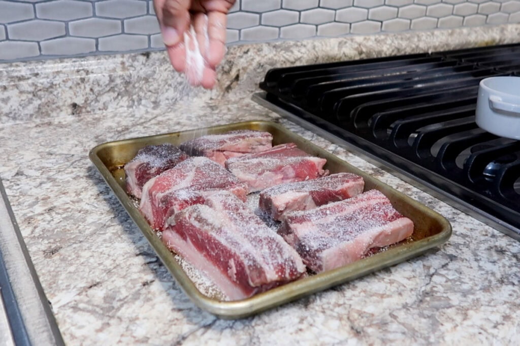 Seasoning short ribs with kosher salt.