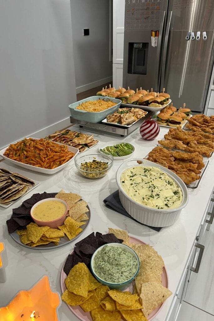 Dinner Party Spread of sliders, mac and cheese, chicken quesadillas, vegan quesadillas, penne alla vodka, chips and queso, and spinach dip, mashed potatoes, and chicken tenders.
